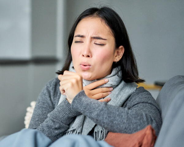 Woman experiencing flu symptoms such as sore throat and coughing